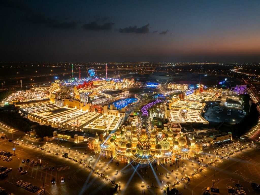 A vibrant cultural pavilion lit up at night in Global Village Dubai, featuring intricate designs and colorful lights.