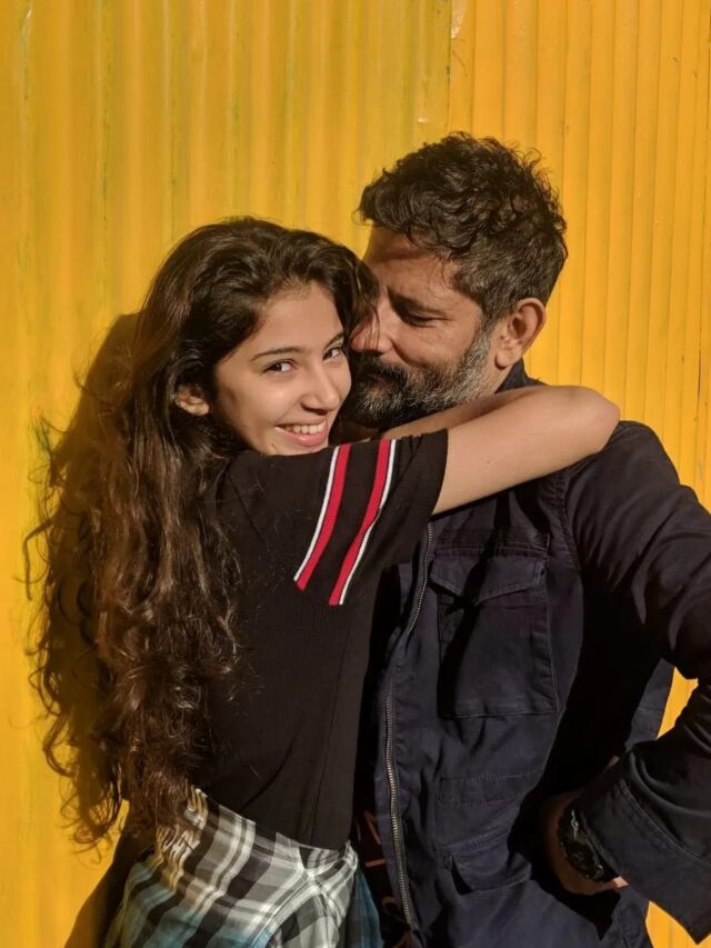 Sara Arjun smiling and hugging a bearded man in front of a yellow background.